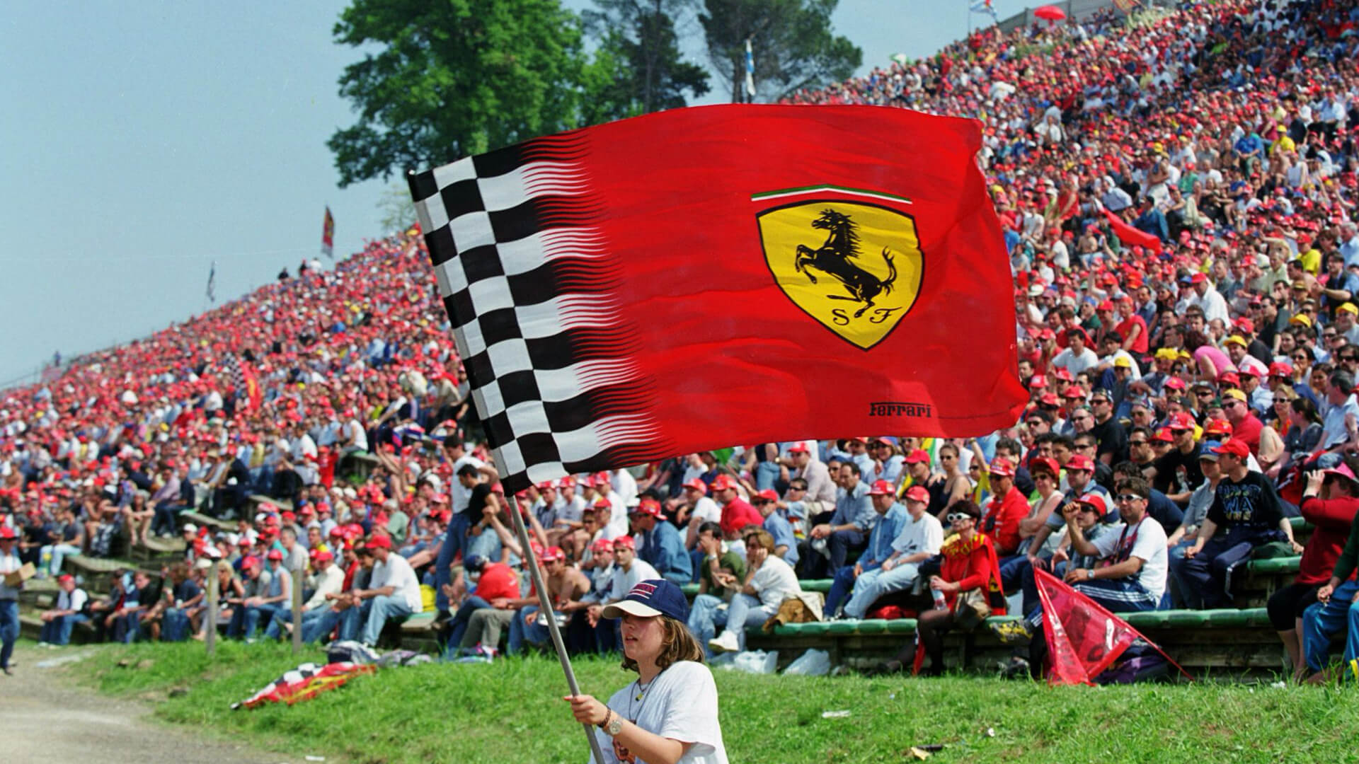 photo of red flag with their Ferrari waved by little girl standing with blue cap and behind her stands packed with people