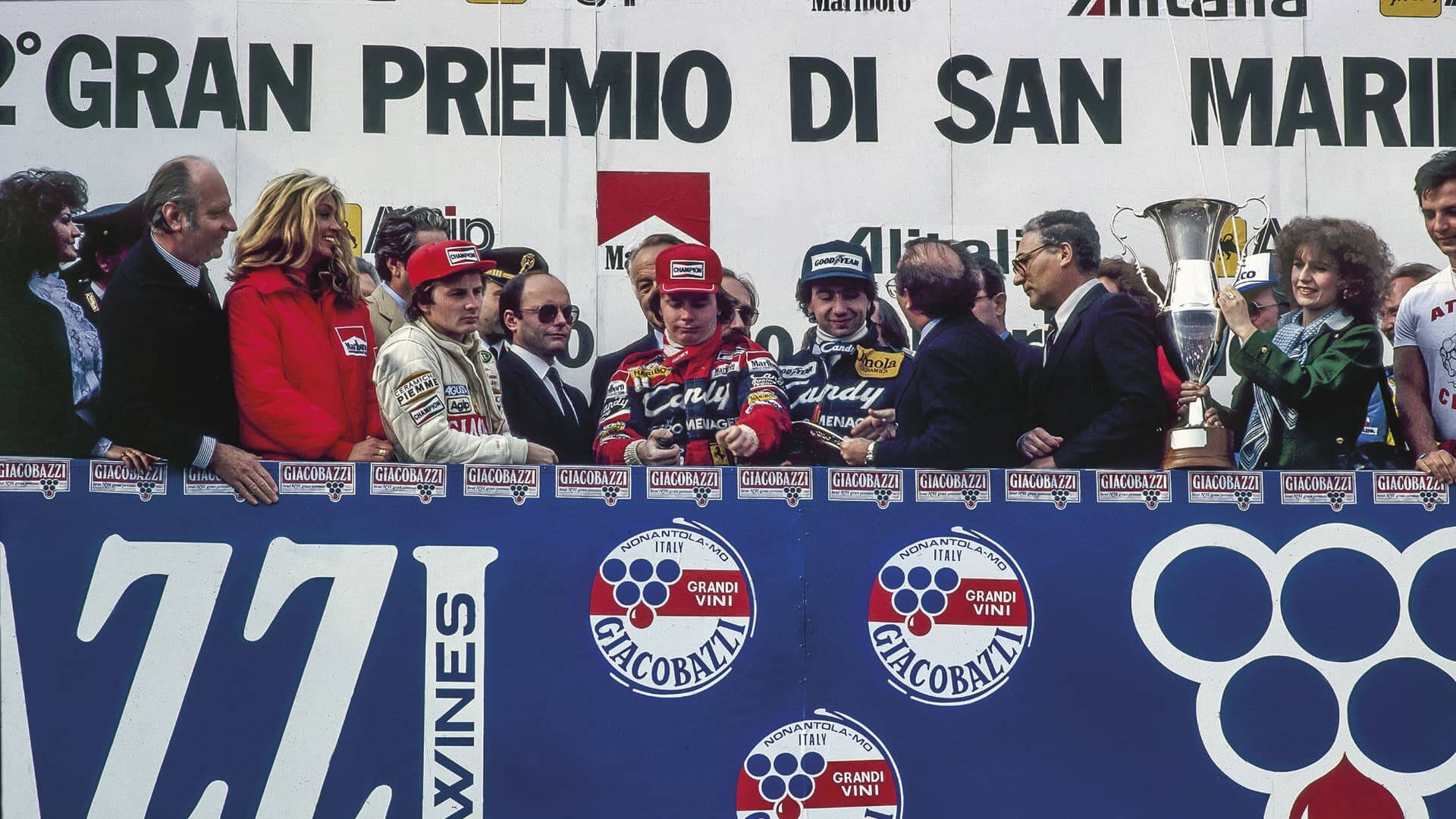 Photo of Pironi and Villeneuve on the podium as he is presented with a Formula 1 GP award at the Imola Autodrome.