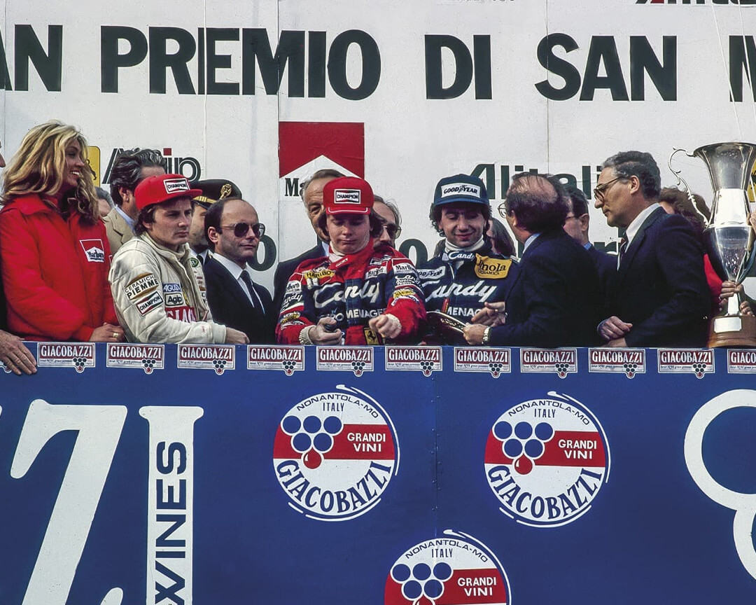 Photo of Pironi and Villeneuve on the podium as he is presented with a Formula 1 GP award at the Imola Autodrome.