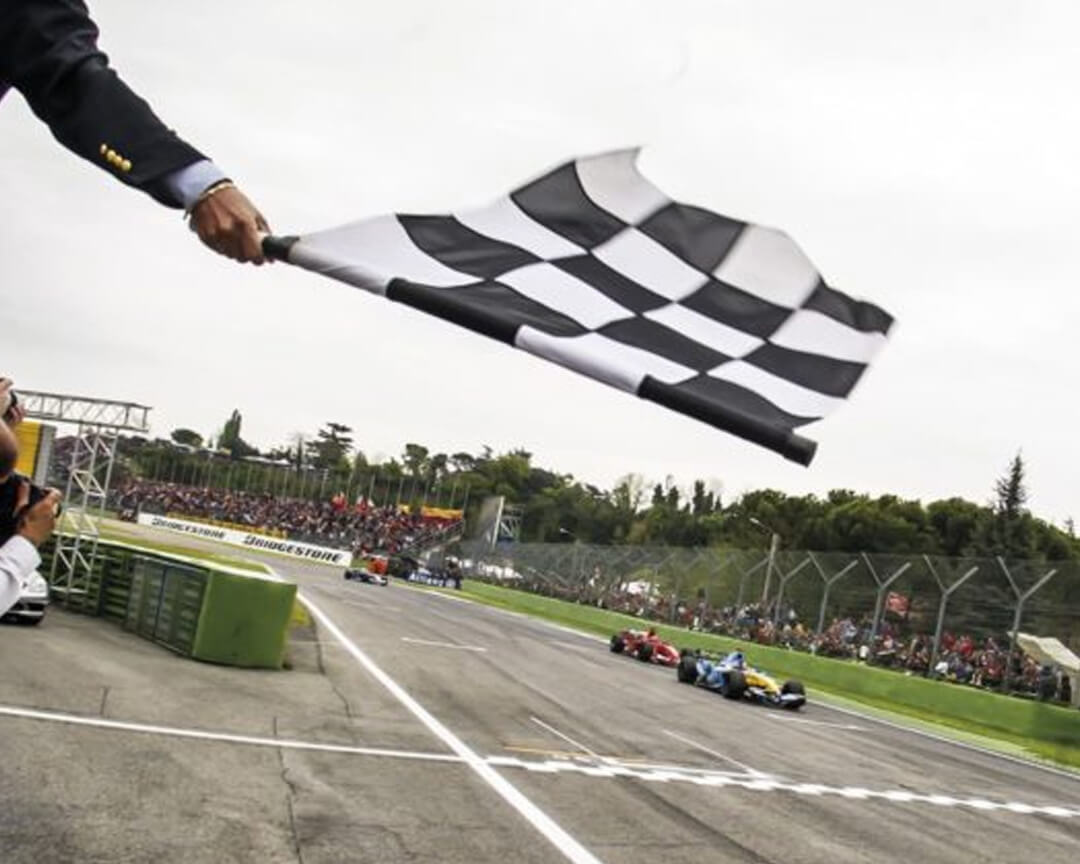 In the foreground, a checkered flag waving at the finish line of a formula one grand prix