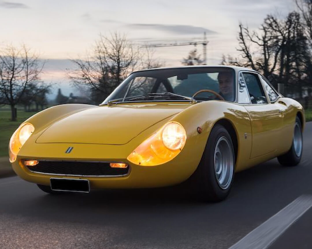 De Tomaso vallelunga in colorazione gialla che sfreccia a fari accesi su una strada