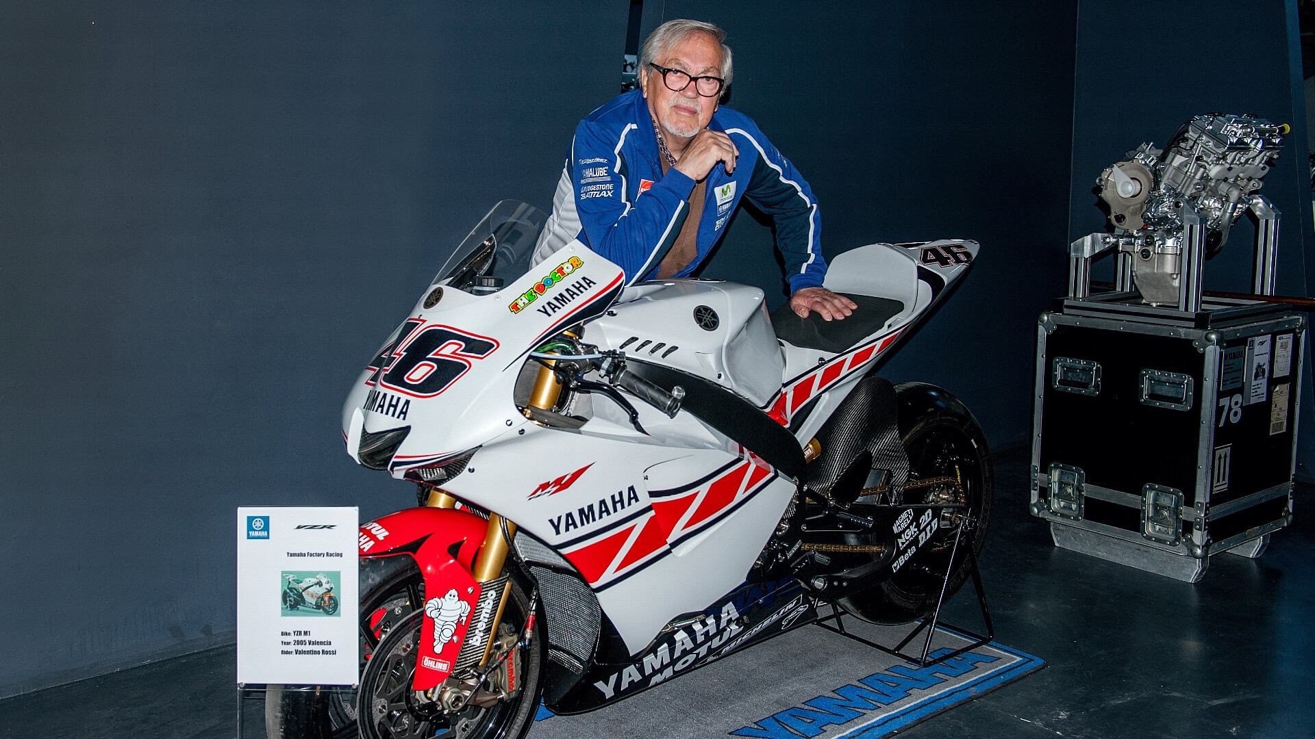 ritratto di Pierluigi Poggi a fianco di una Yamaha da corsa di Valentino Rossi bianca e un motore sullo sfondo