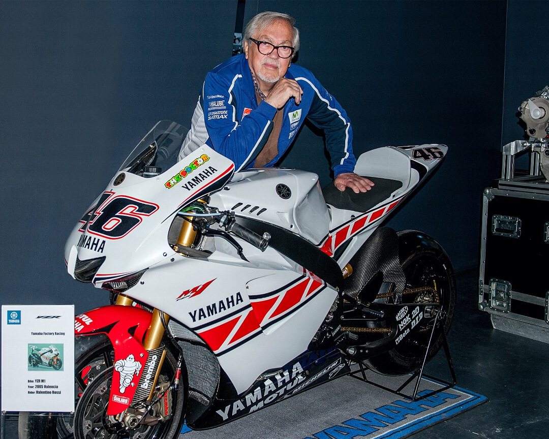 ritratto di Pierluigi Poggi a fianco di una Yamaha da corsa di Valentino Rossi bianca e un motore sullo sfondo