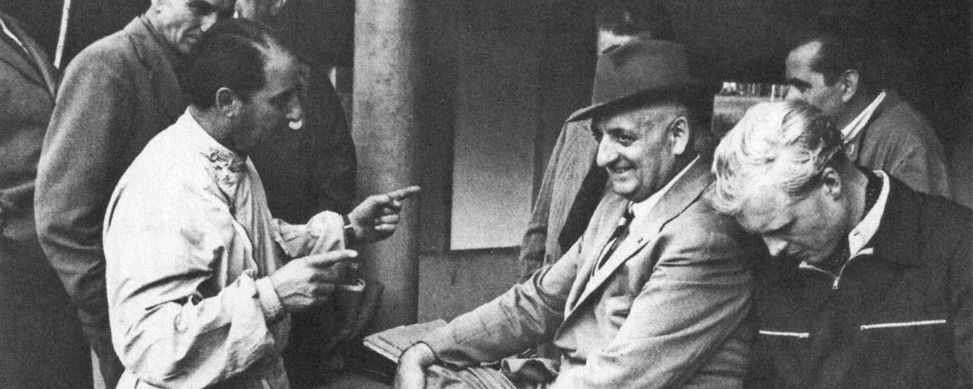 foto d'epoca di Enzo Ferrari che sorride con tecnici e meccanici
