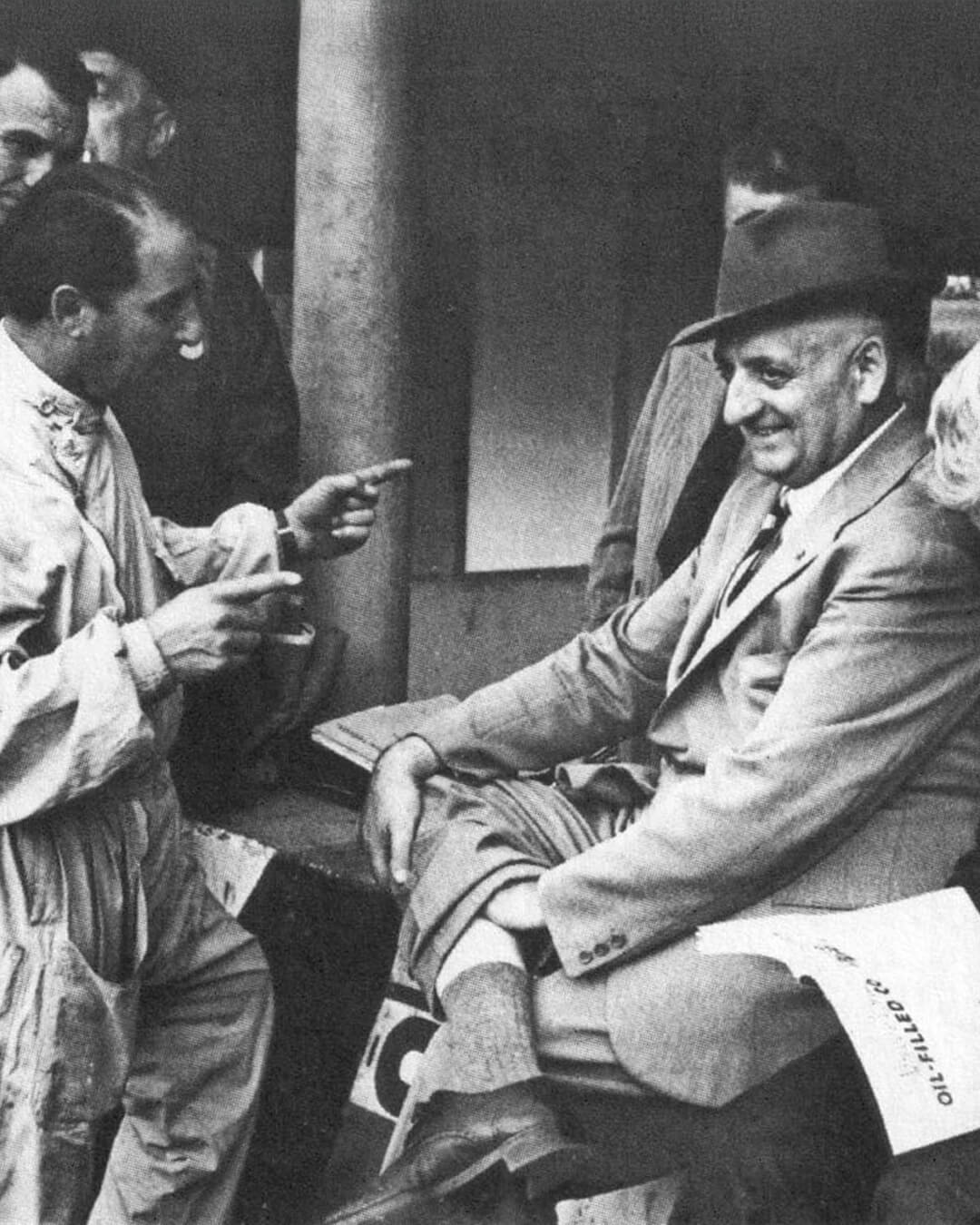 foto d'epoca di Enzo Ferrari che sorride con tecnici e meccanici
