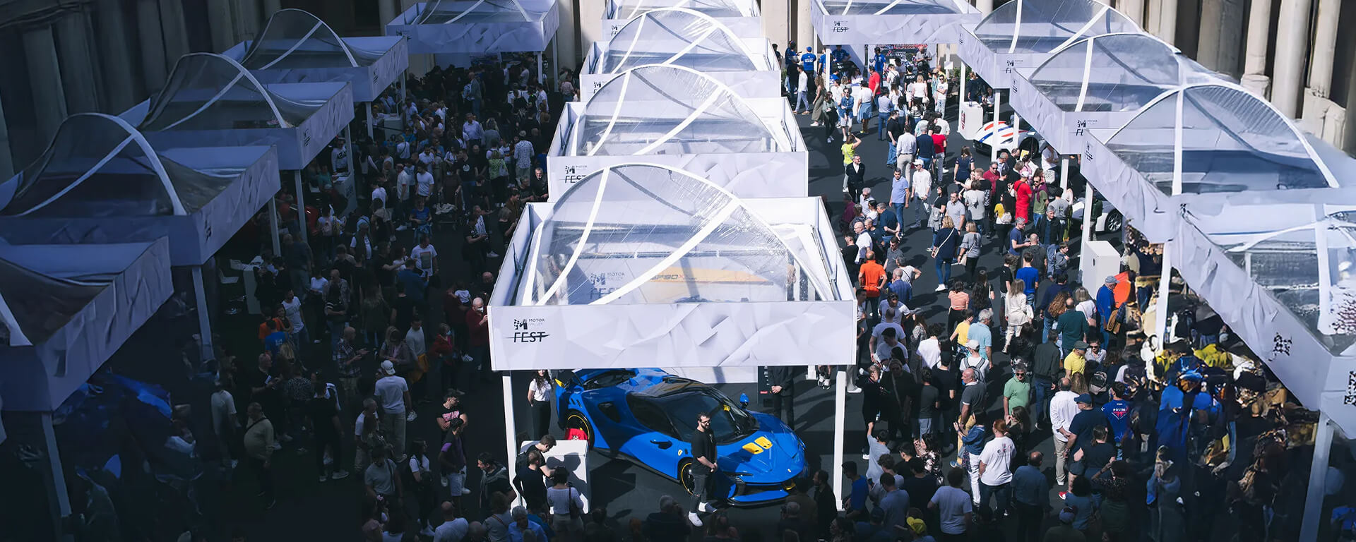 piazza con molte persone attorno a gazebo bianchi con automobili in esposizione