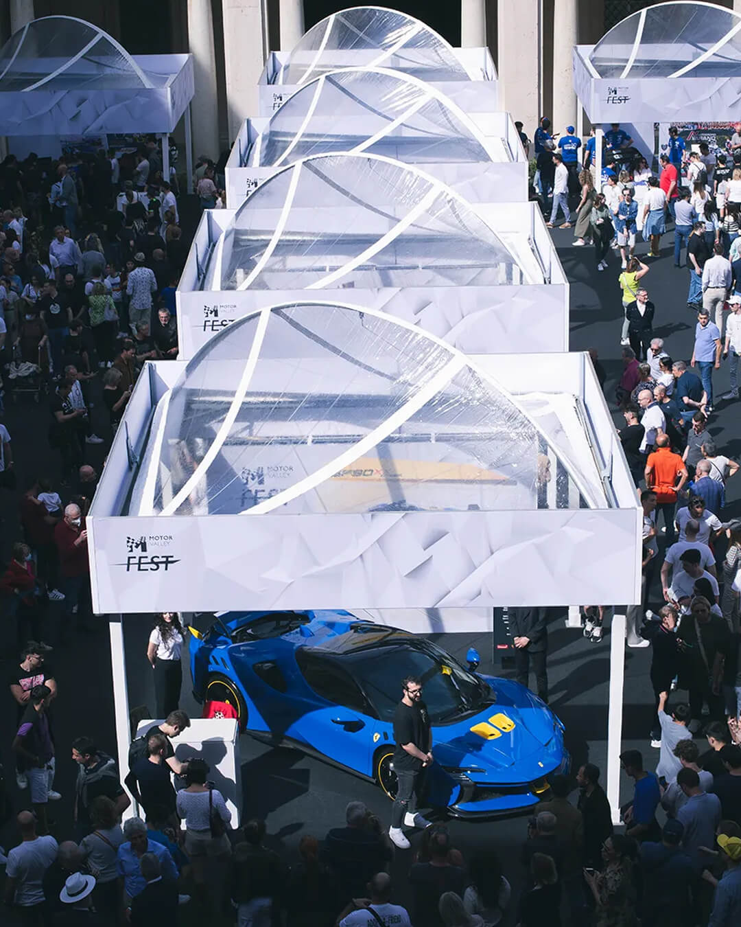 piazza con molte persone attorno a gazebo bianchi con automobili in esposizione