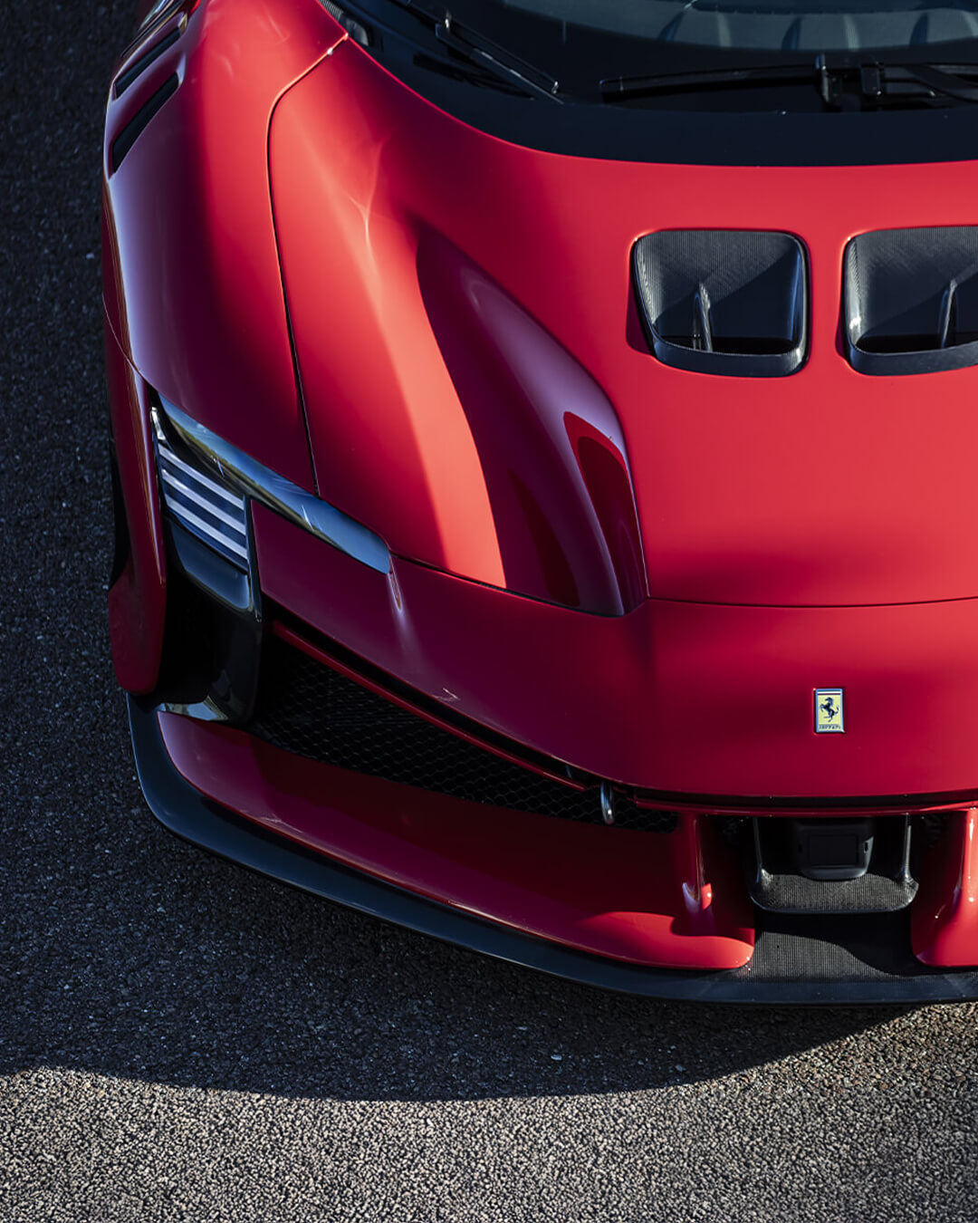 muso di una Ferrari supercar rossa dall'alto con asfalto