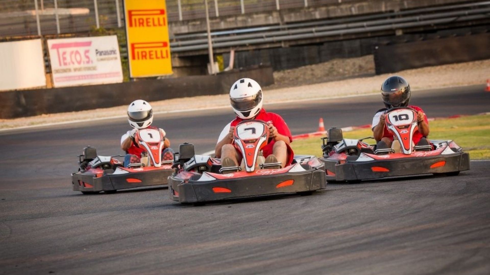 Tre piloti alla guida di go-kart rossi e neri in corsa ravvicinata sull'asfalto di una pista automobilistica.
