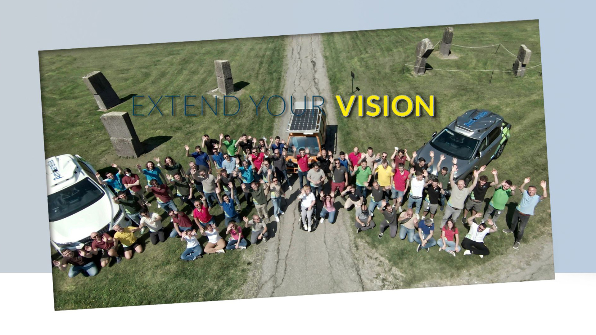 Overhead photo of group of young people with their hands turned towards the sky, 3 cars parked behind them and the inscription Extend your vision