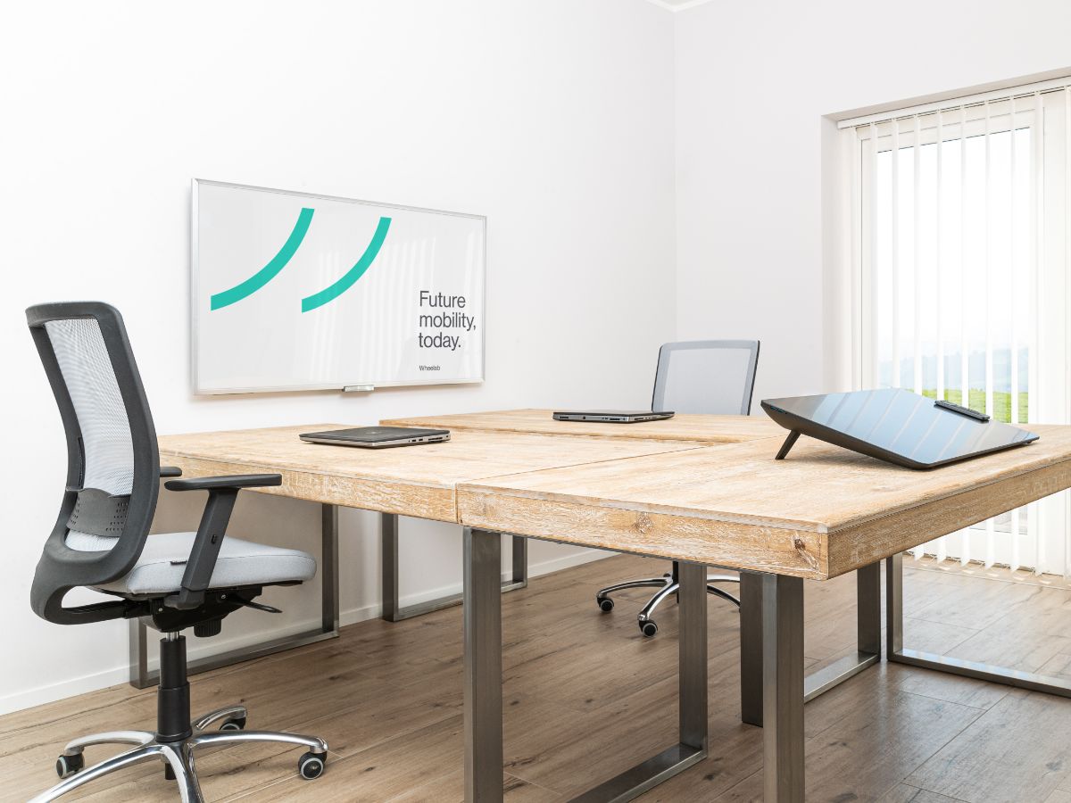 Ufficio di Wheelab, monitor al muro, tablet sul tavolo di legno, porta finestra che lascia intravedere uno spazio verde.