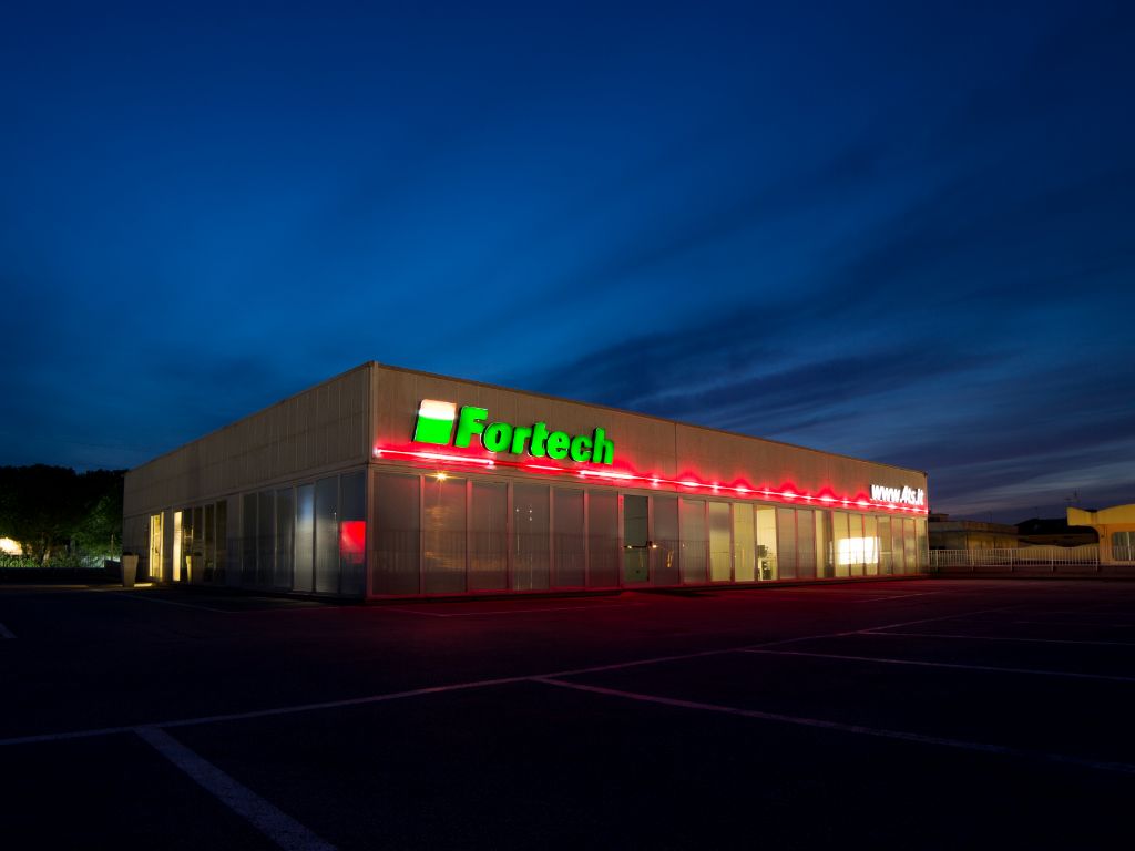 Capannone della Fortech da fuori di sera con l'insegna illuminata.