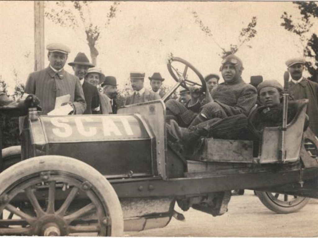 Francesco Stanguellini a bordo di un'auto d'epoca, circondato da delle persone.