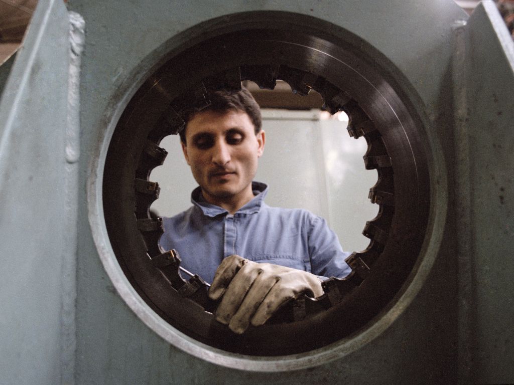 Operaio con guanto al lavoro, visto attraverso un buco di un macchinario.