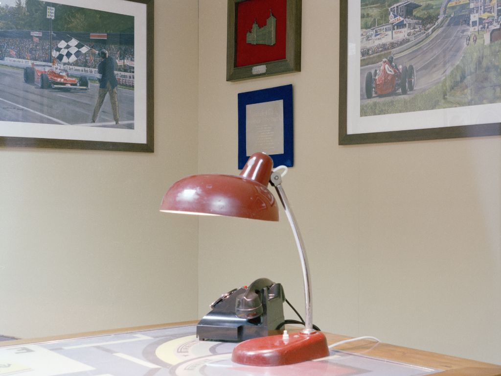 Lampada rossa e vecchio telefono su una scrivania di un ufficio. Si intravedono quadri alle pareti.