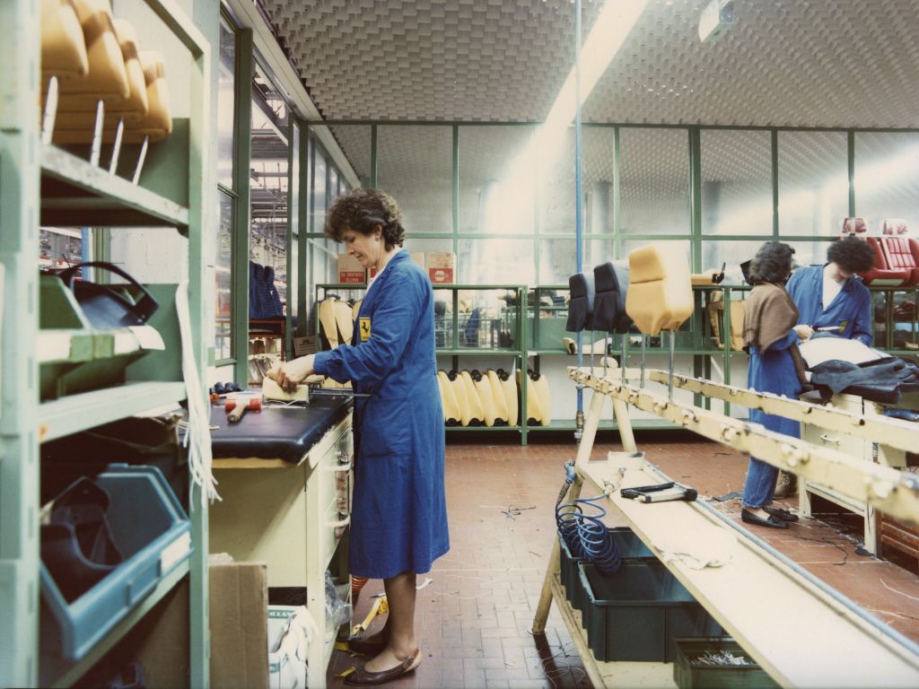 Operaia con un camice blu al lavoro, di profilo, all'interno dello stabilimento di Maranello.