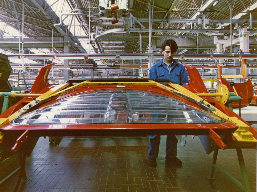 Operaio con camice blu che lavora un pezzo della carrozzeria di una Ferrari, all'interno di una fabbrica.