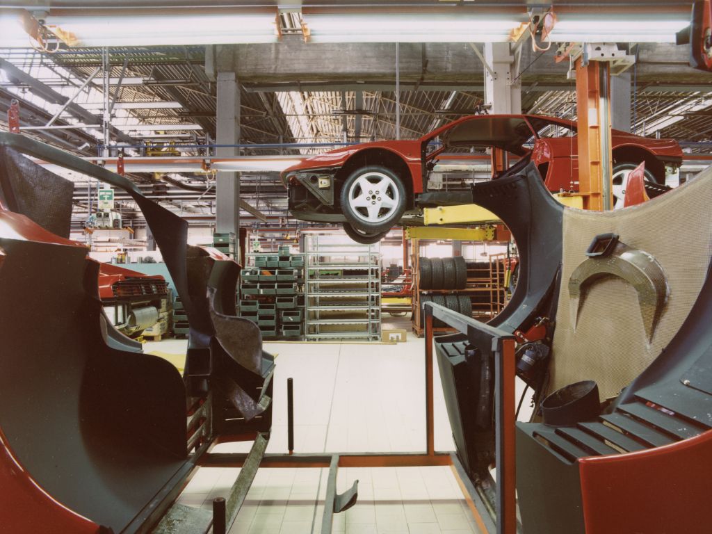 Interni della fabbrica della Ferrari: si intravede una vettura issata in alto da un macchinario, e scaffali di pneumatici.