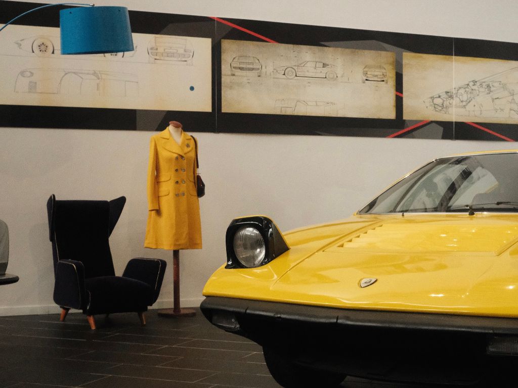 Una Lamborghini esposta a fianco di un cappotto, ad una sedia e ad una lampada vintage presso il Museo Ferruccio Lamborghini.