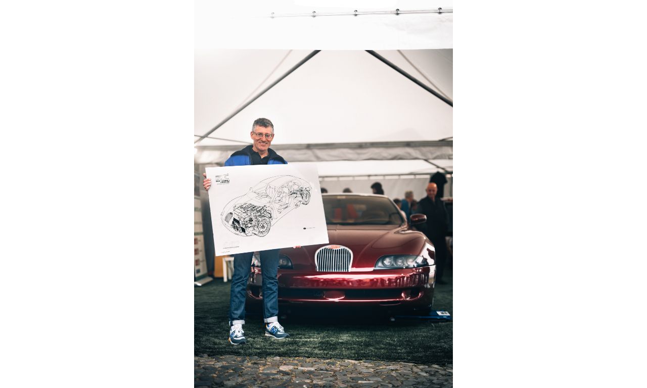 Un uomo con un disegno meccanico di una Bugatti posa di fianco al modello reale.