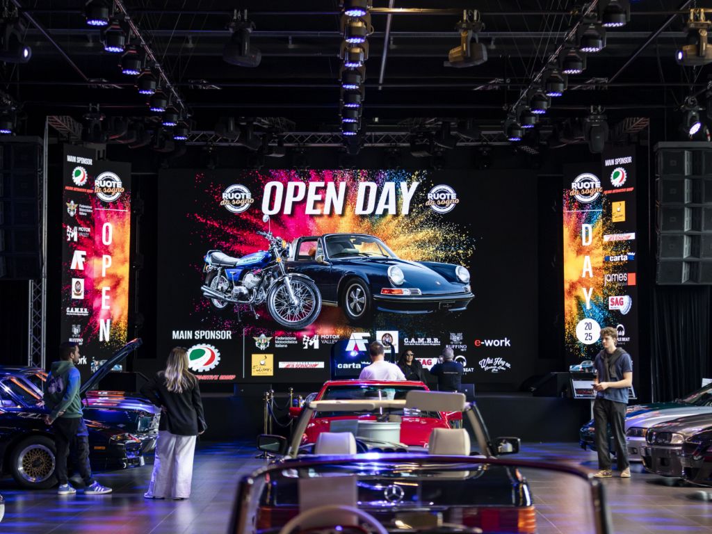 Interni di Ruote da Sogno, con persone, vetture e cartellone dell'Open Day.