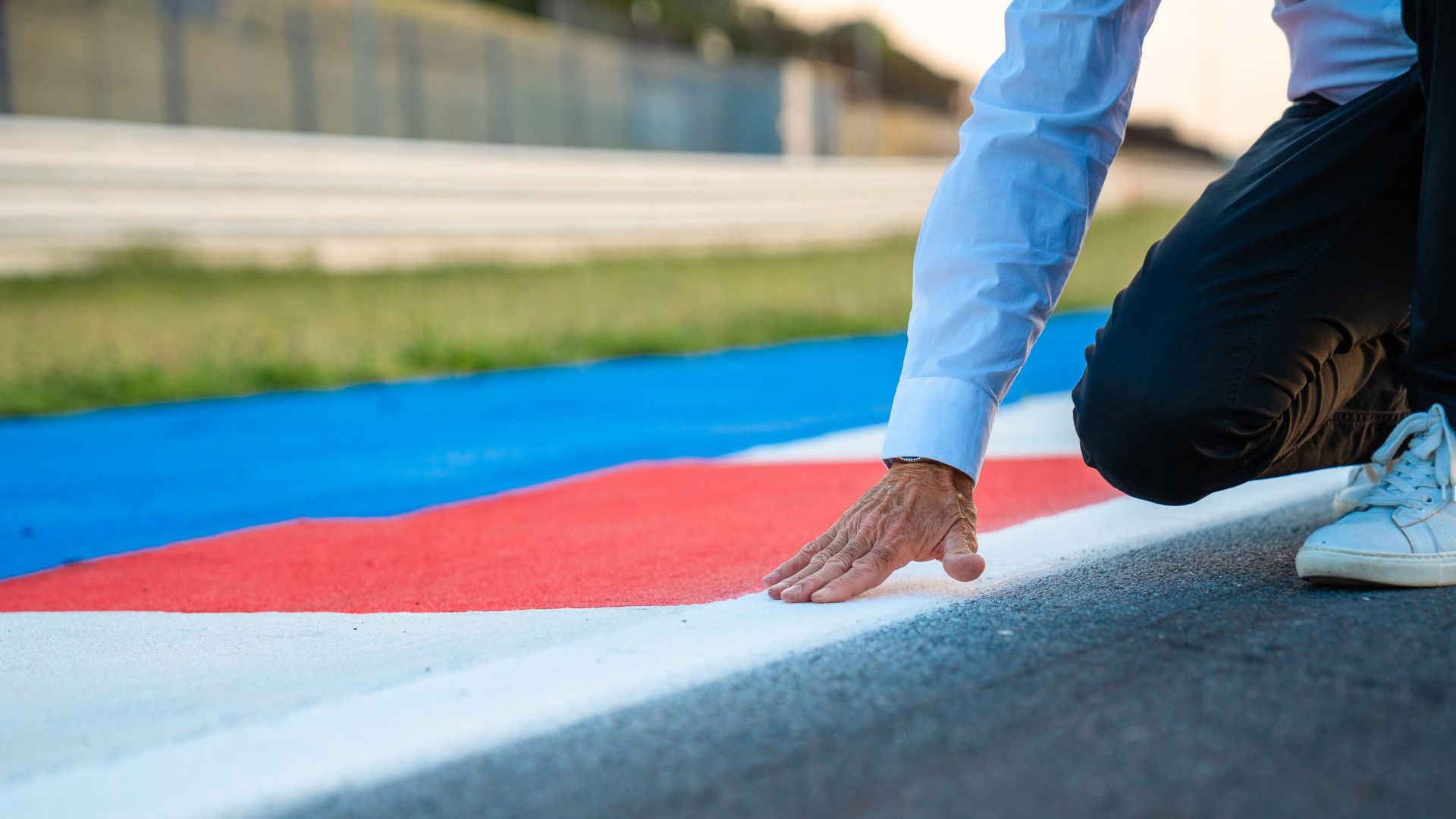 Una mano tocca l'asfalto del cordolo di un circuito, dipinto con le vernici di Colorificio Sammarinese.
