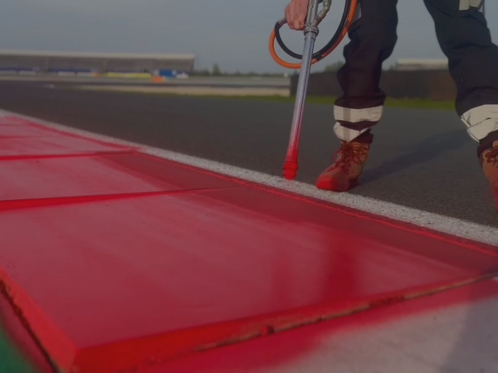 Un tecnico di Colorificio Sammarinese dipinge i cordoli di un circuito con un aerografo.