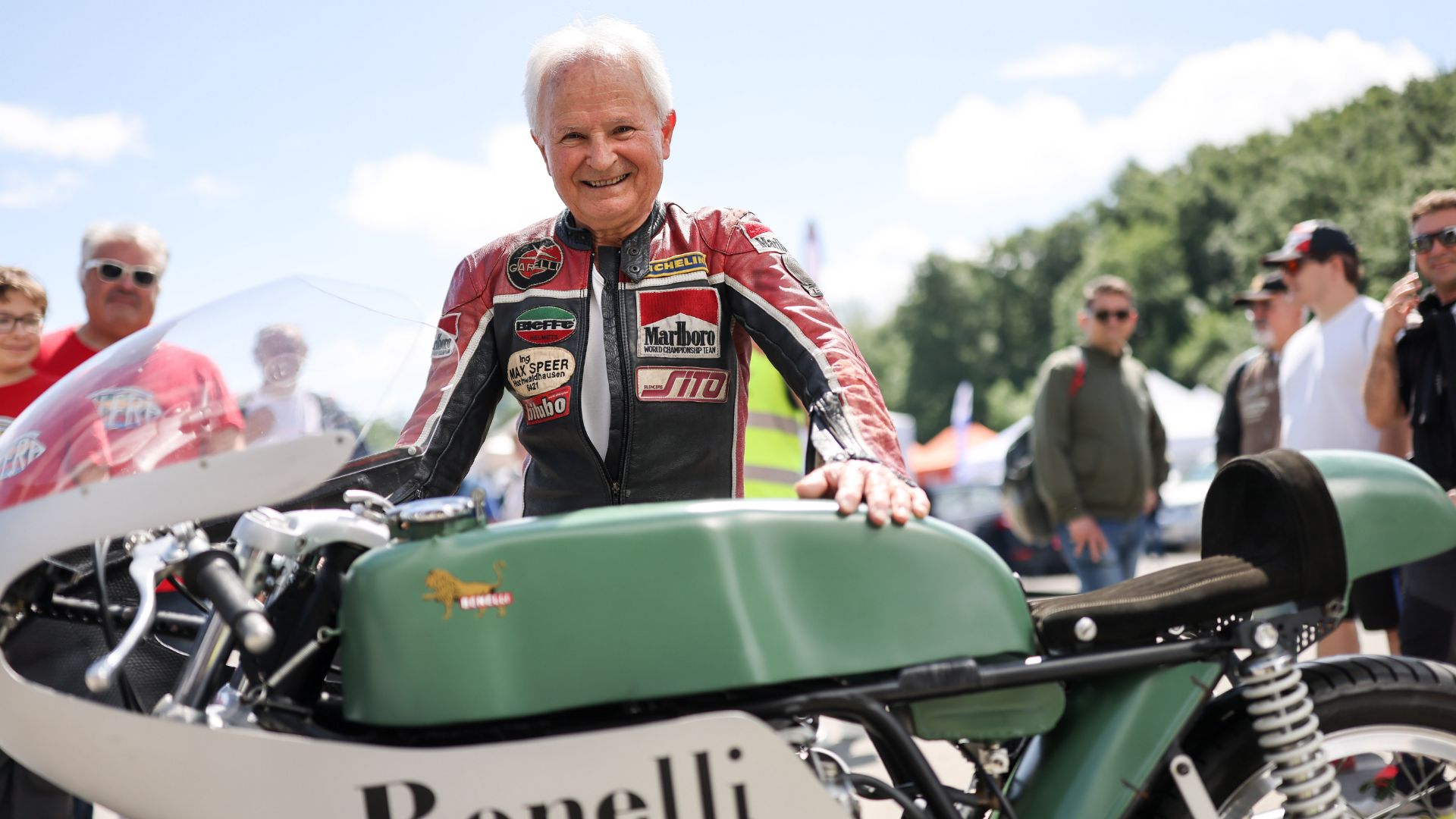 Anziano signore con la tuta da motociclista accarezza la sua moto storica.