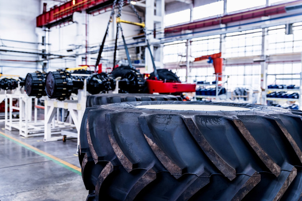 Interno di un’officina meccanica con grandi pneumatici agricoli in primo piano e componenti di assi in lavorazione sullo sfondo.