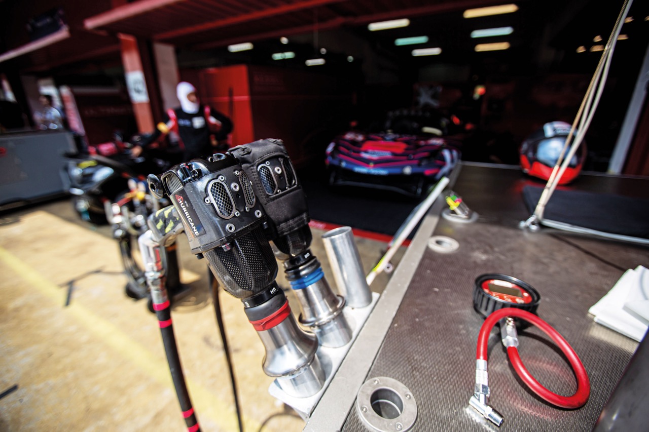 Primo piano di due avvitatori pneumatici Paoli Hurricane riposti in un supporto nel box, con un'auto da corsa sfocata sullo sfondo.