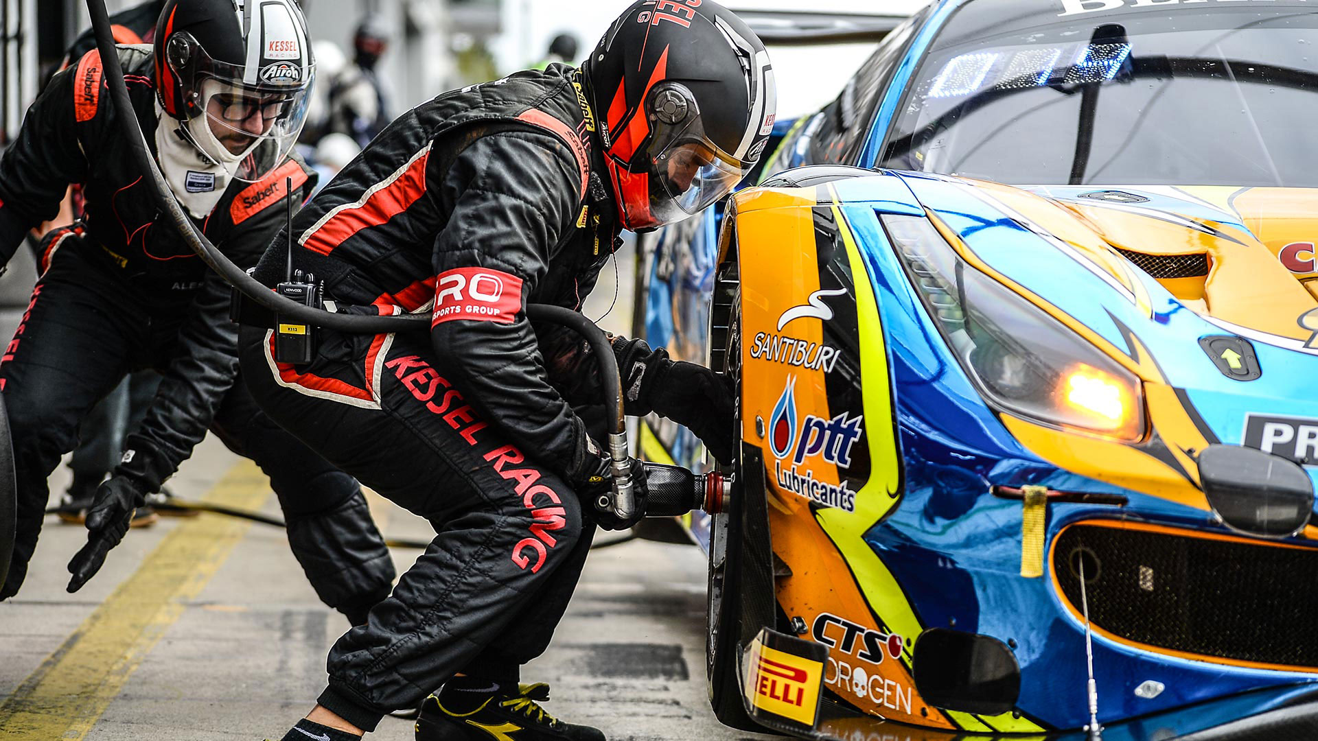 Meccanici del team Kessel Racing durante un cambio gomme rapido su una Ferrari da competizione gialla e blu.
