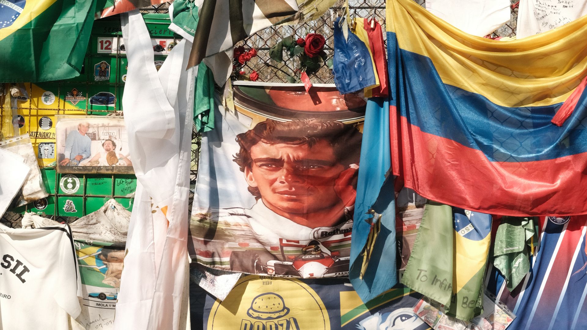 Bandiere del Brasile e della Colombia accanto a un poster di Ayrton Senna su una recinzione commemorativa.