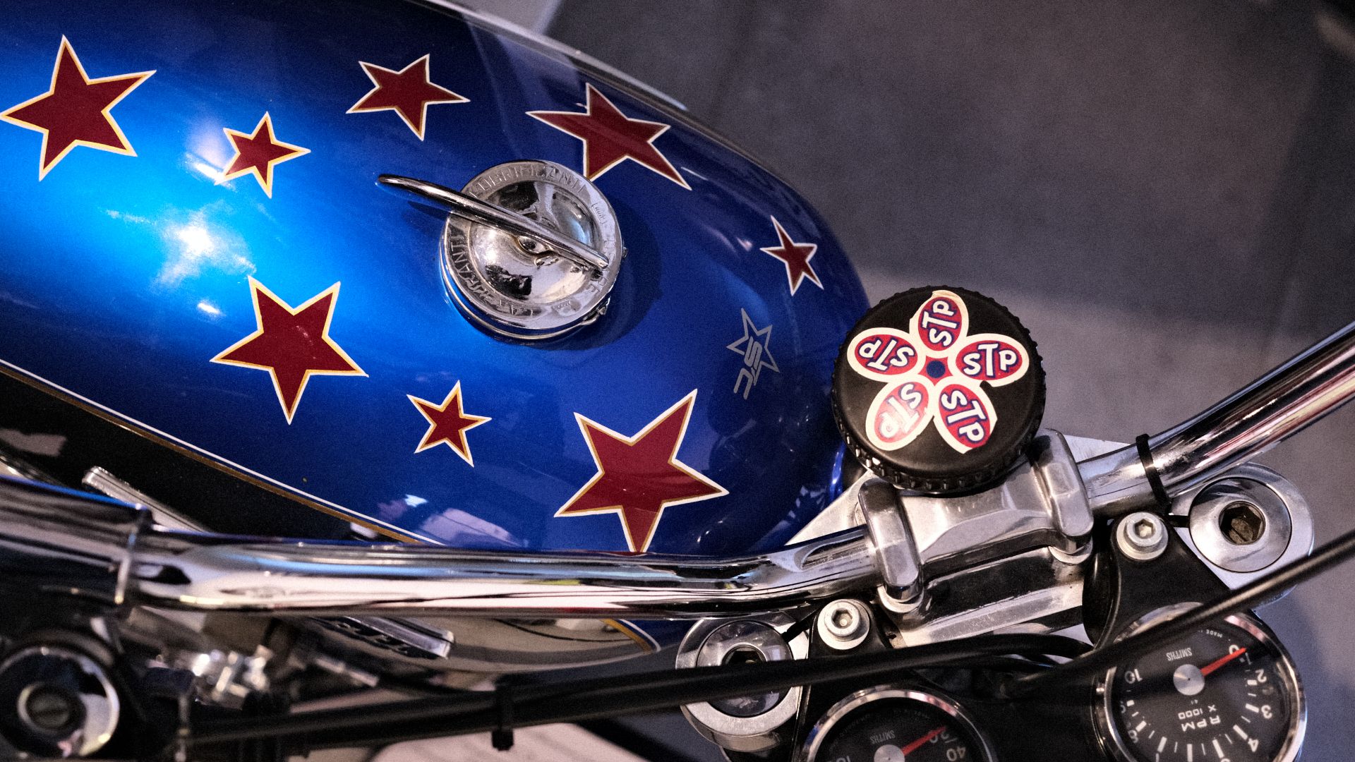 Primo piano del serbatoio blu metallizzato con stelle rosse della Ducati Scrambler appartenuta a Lucio Dalla, con tappo STP personalizzato, esposta presso Rino's Garage.