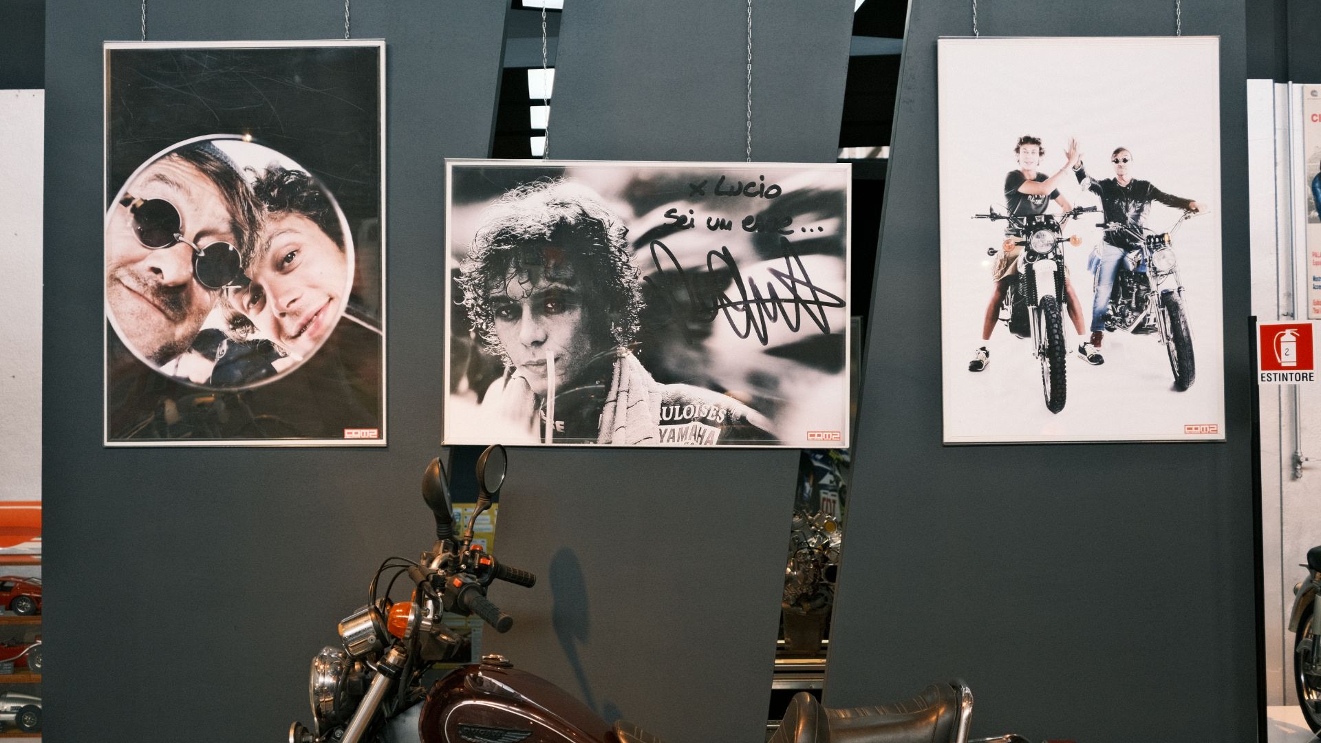 Tre poster incorniciati su una parete scura che ritraggono Valentino Rossi e Lucio Dalla sopra una moto d'epoca