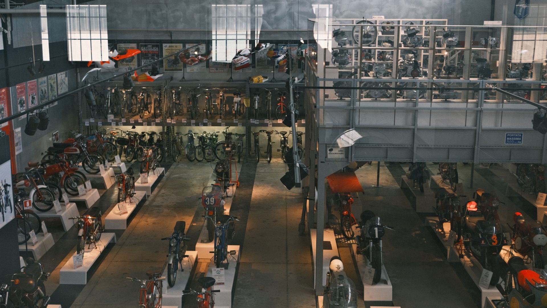 Veduta dall'alto di un'ampia esposizione di motociclette d'epoca disposte su pedane bianche nella Collezione Moto Poggi.