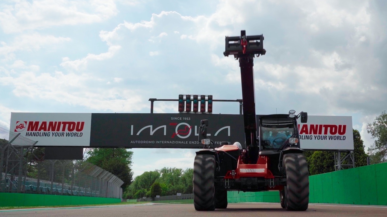 Sollevatore telescopico Manitou con braccio esteso in verticale sulla pista dell'Autodromo di Imola, posizionato sotto il ponte del traguardo brandizzato Manitou.