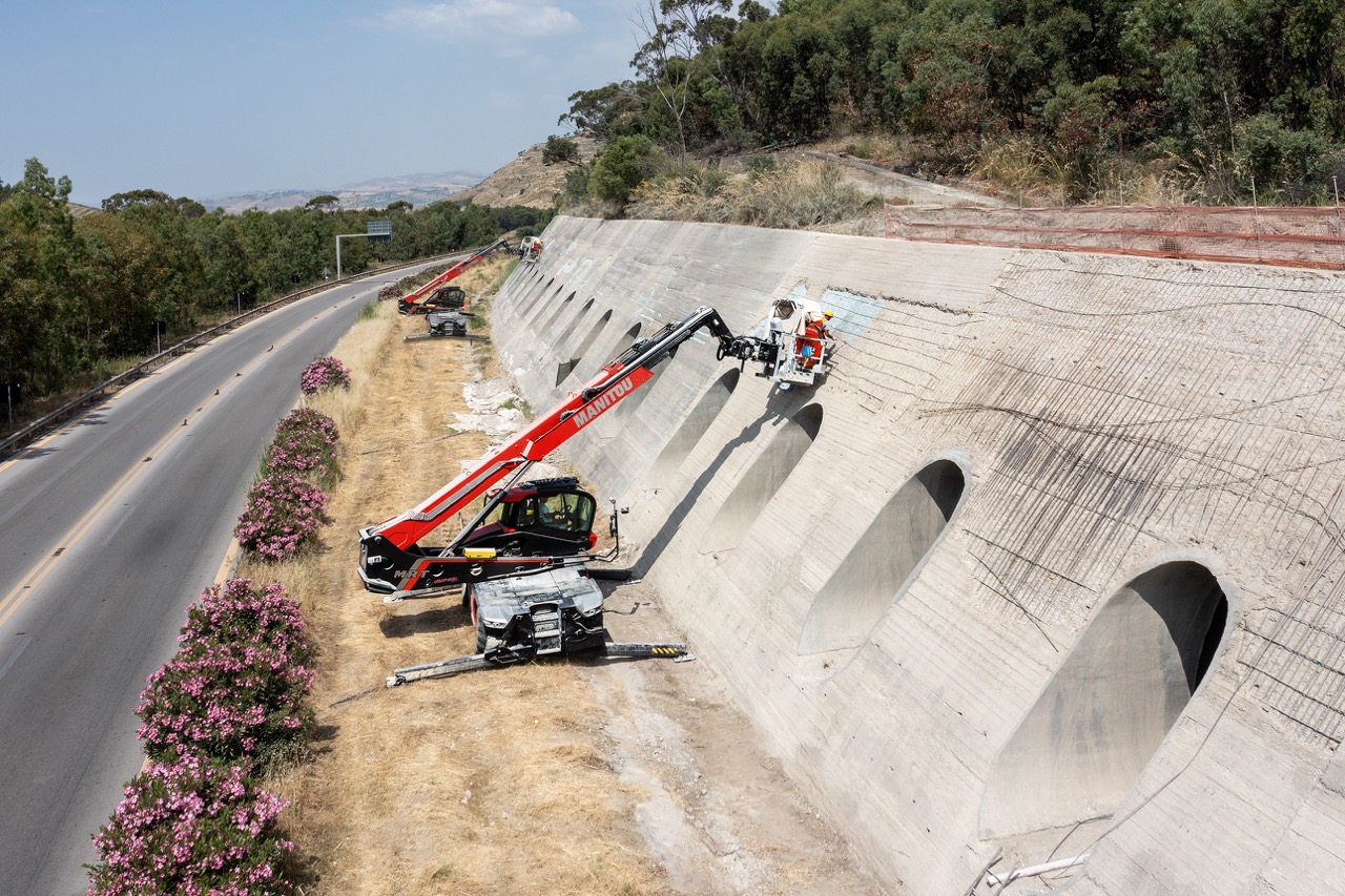 Sollevatore telescopico rotativo Manitou MRT con piattaforma porta-persone utilizzato per lavori di manutenzione e ripristino di un muro di contenimento autostradale.