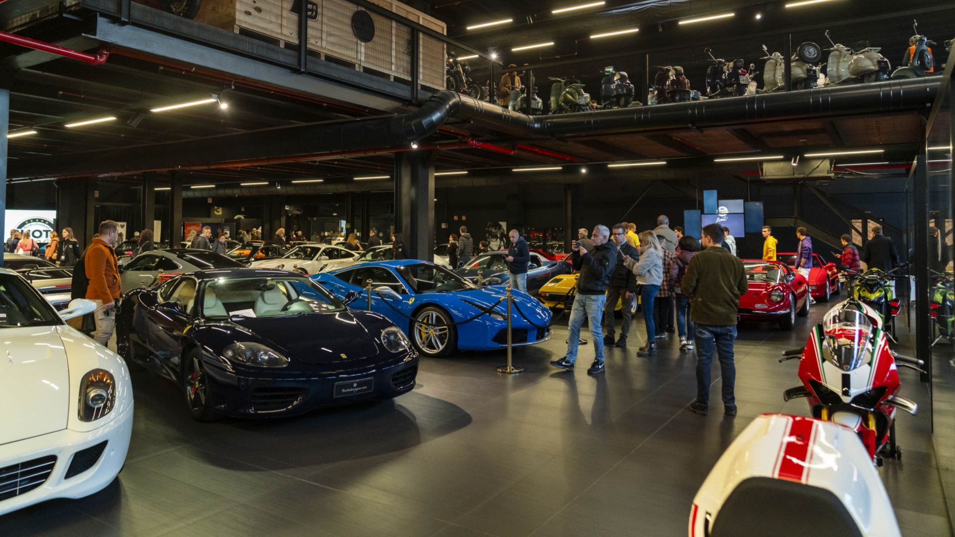 Interni dello showroom Ruote da Sogno a Reggio Emilia, con le persone che fotografano le auto esposte.