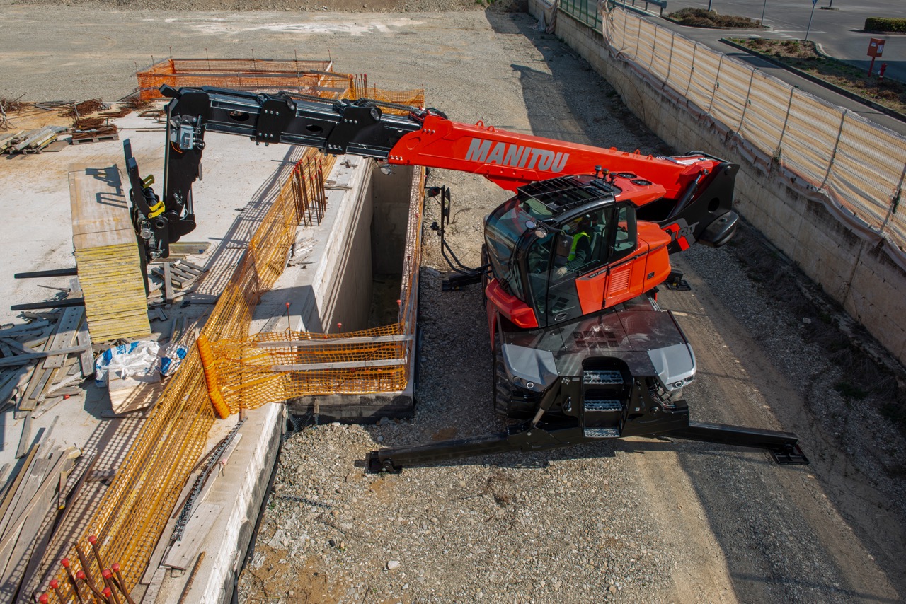 Veduta dall'alto di un sollevatore telescopico rotativo Manitou MRT 2260 impegnato nella movimentazione di materiali sopra uno scavo di fondazione in un cantiere edile.