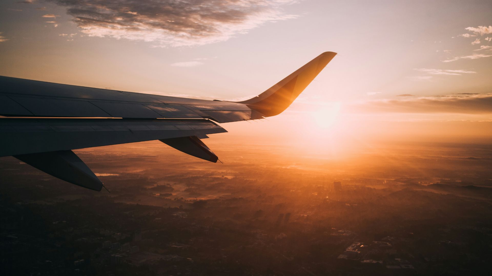 Ala di un aereo in volo al tramonto sopra una città.
