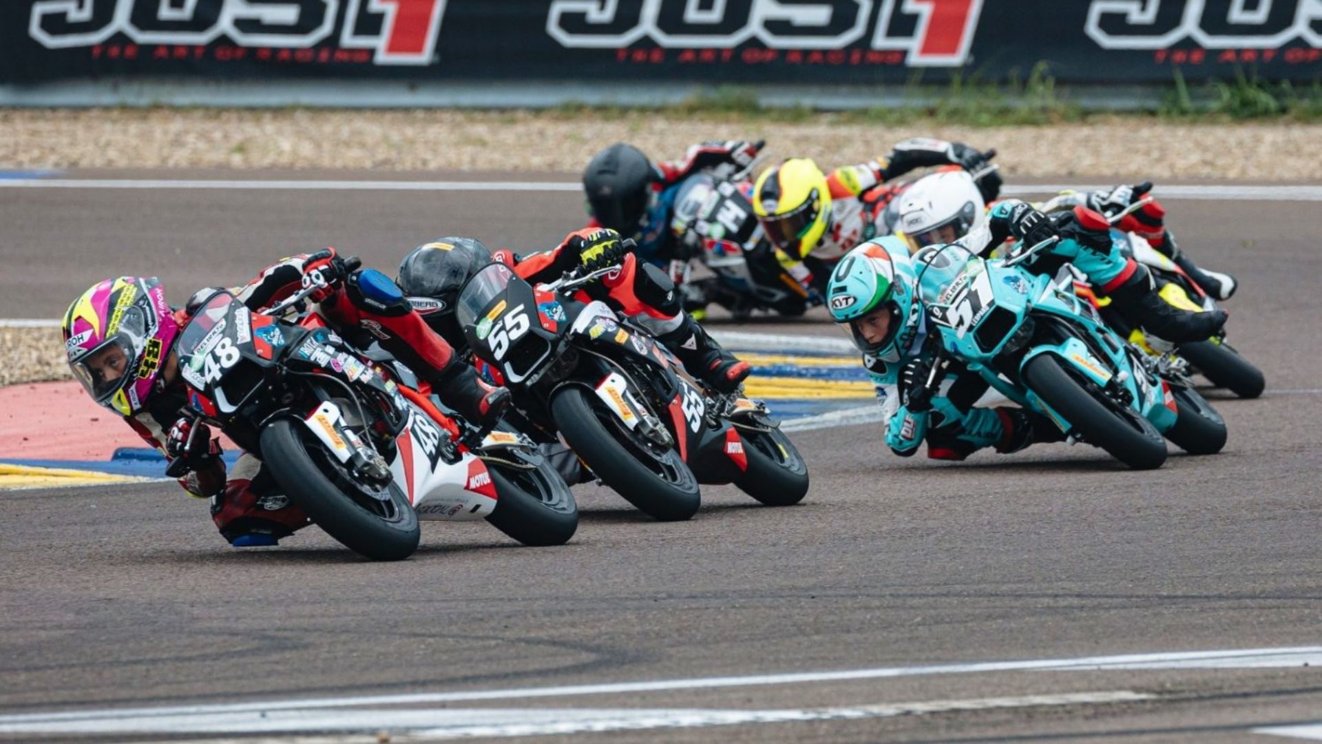 Un gruppo compatto di piloti in sella a mini-moto da corsa mentre affrontano una curva a gomito su un circuito asfaltato.