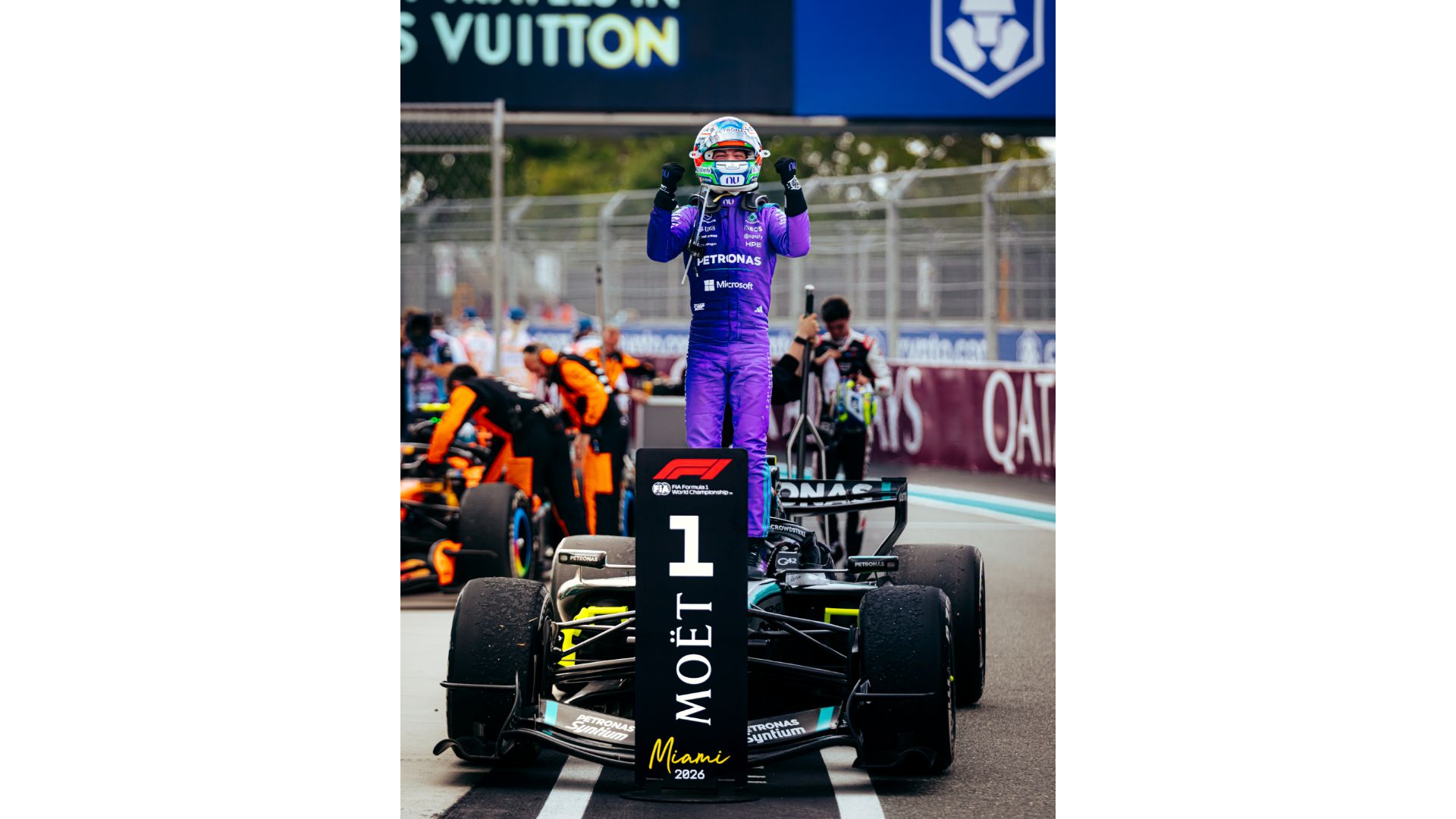 Inquadratura frontale di Kimi Antonelli che esulta in piedi sulla sua Mercedes numero 12 dopo la vittoria. Ha le braccia alzate e i pugni chiusi. Davanti all'auto è posizionato il cartello "P1" di Moët & Chandon con la scritta "Miami 2026".