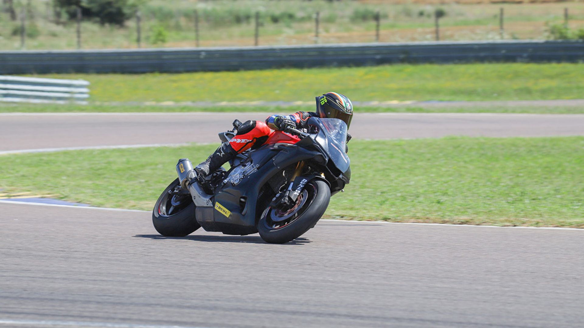 Un motociclista in sella a una moto sportiva nera mentre affronta una piega a destra su un circuito automobilistico in una giornata di sole.