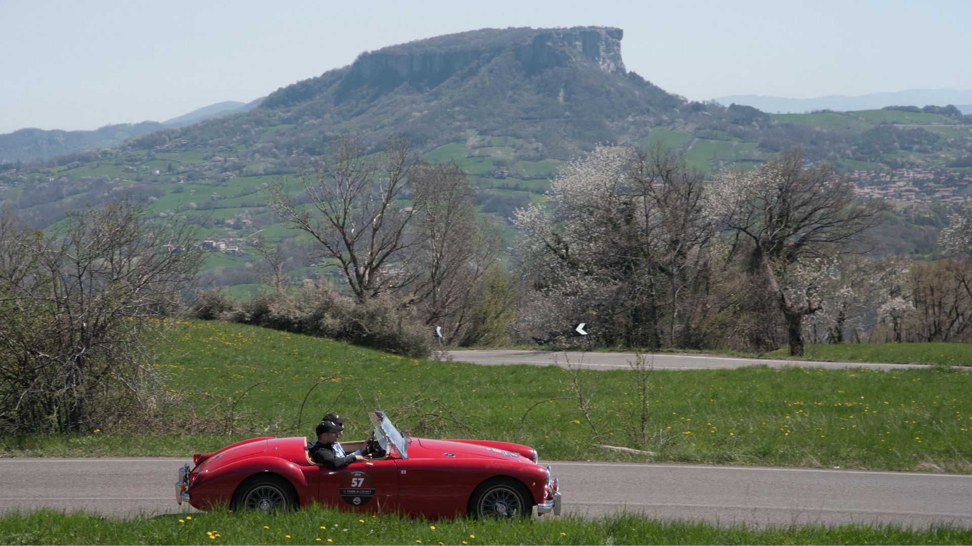 Auto d'epoca rossa durante il rally Terre di Canossa con lo sfondo della Pietra di Bismantova nell'Appennino Reggiano.