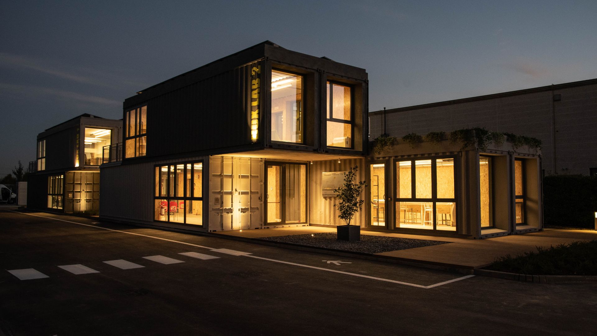 Vista notturna illuminata dei laboratori di ricerca Box Lab, architettura modulare con container convertiti e luce calda dagli interni