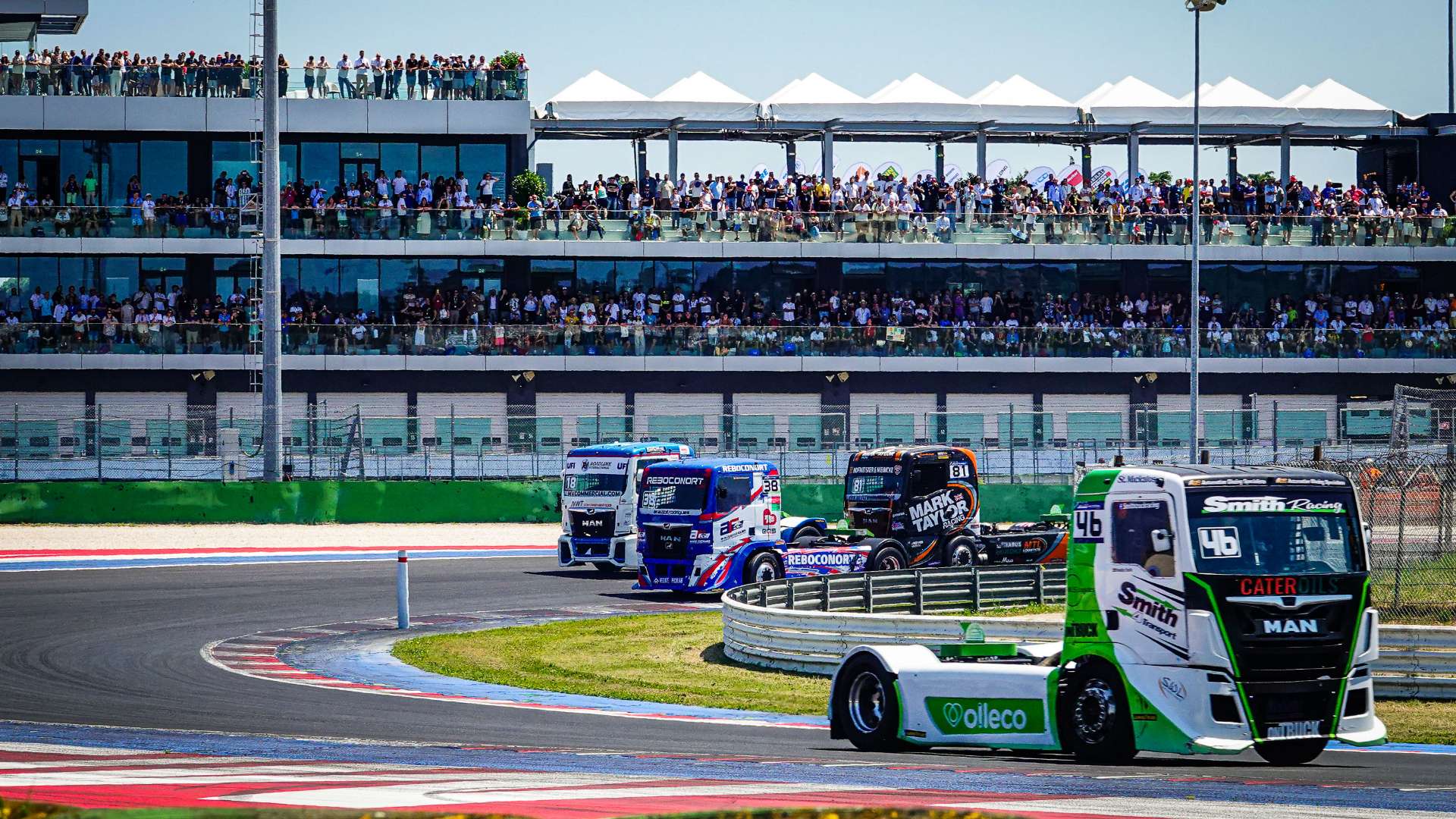 Camion da corsa in pista al Misano World Circuit durante il Misano Grand Prix Truck, con le terrazze del paddock affollate di spettatori.
