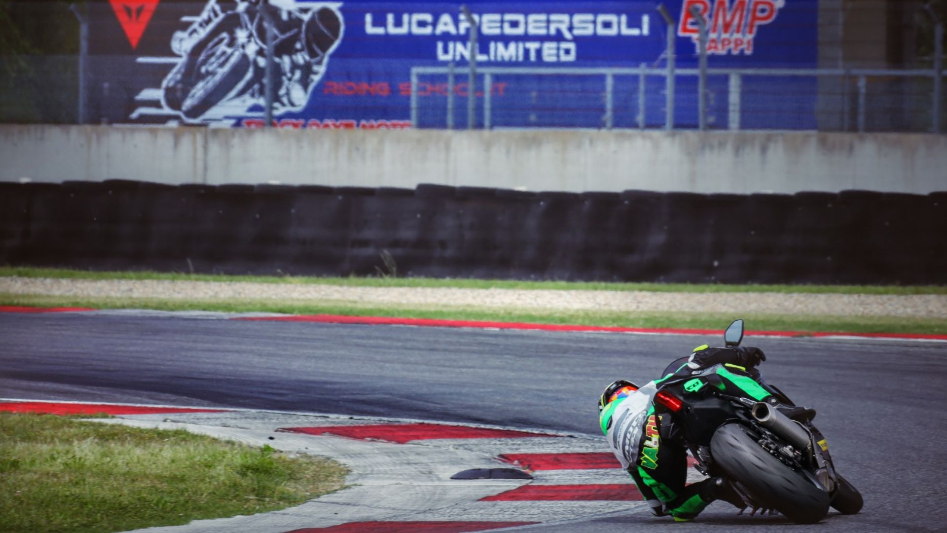 Pilota di moto da corsa in piega estrema in curva sul cordolo della pista.