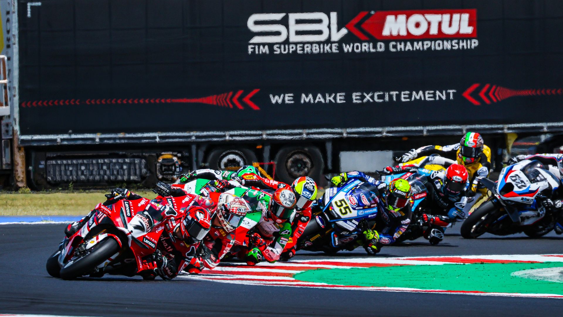 Gruppo compatto di piloti in sella a moto da corsa che affrontano una curva ravvicinata durante una gara del Campionato Mondiale SBK Motul 2026, sotto lo striscione ufficiale del circuito.
