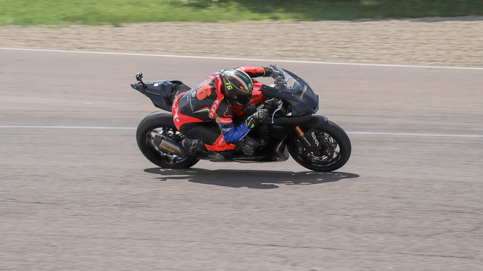 Un motociclista in tuta da gara e casco inclinato in piega su una moto sportiva nera durante un corso della Modena Riding School all'Autodromo di Modena.