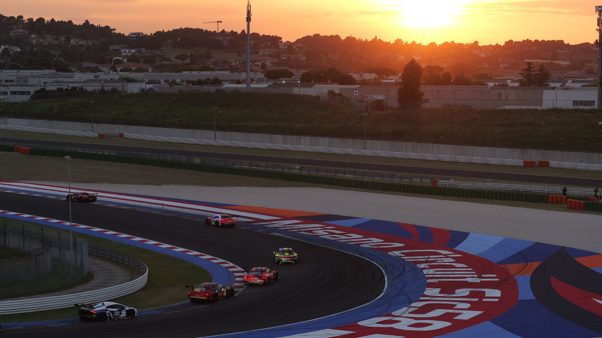 Auto da corsa GT in pista al Misano World Circuit durante una gara serale al tramonto.